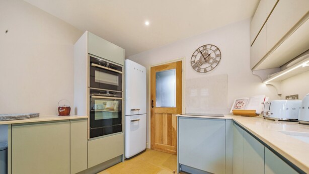Une cuisine moderne dotée d’appareils électroménagers intégrés, d’une porte en bois et d’une horloge murale.
