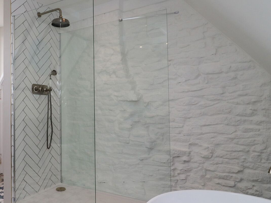 Zona de ducha con mampara de vidrio y un diseño de baldosas en patrón de espiga en la pared.