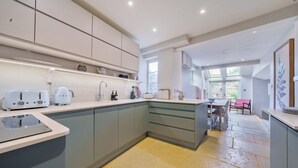 A modern kitchen with grey cabinets, a central island, and a dining area with a red chair. - Lynton Cottage (Chipping Norton)