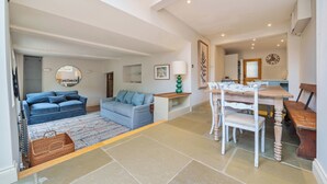 A spacious living area with a sofa, a dining table, and a bench. - Lynton Cottage (Chipping Norton)