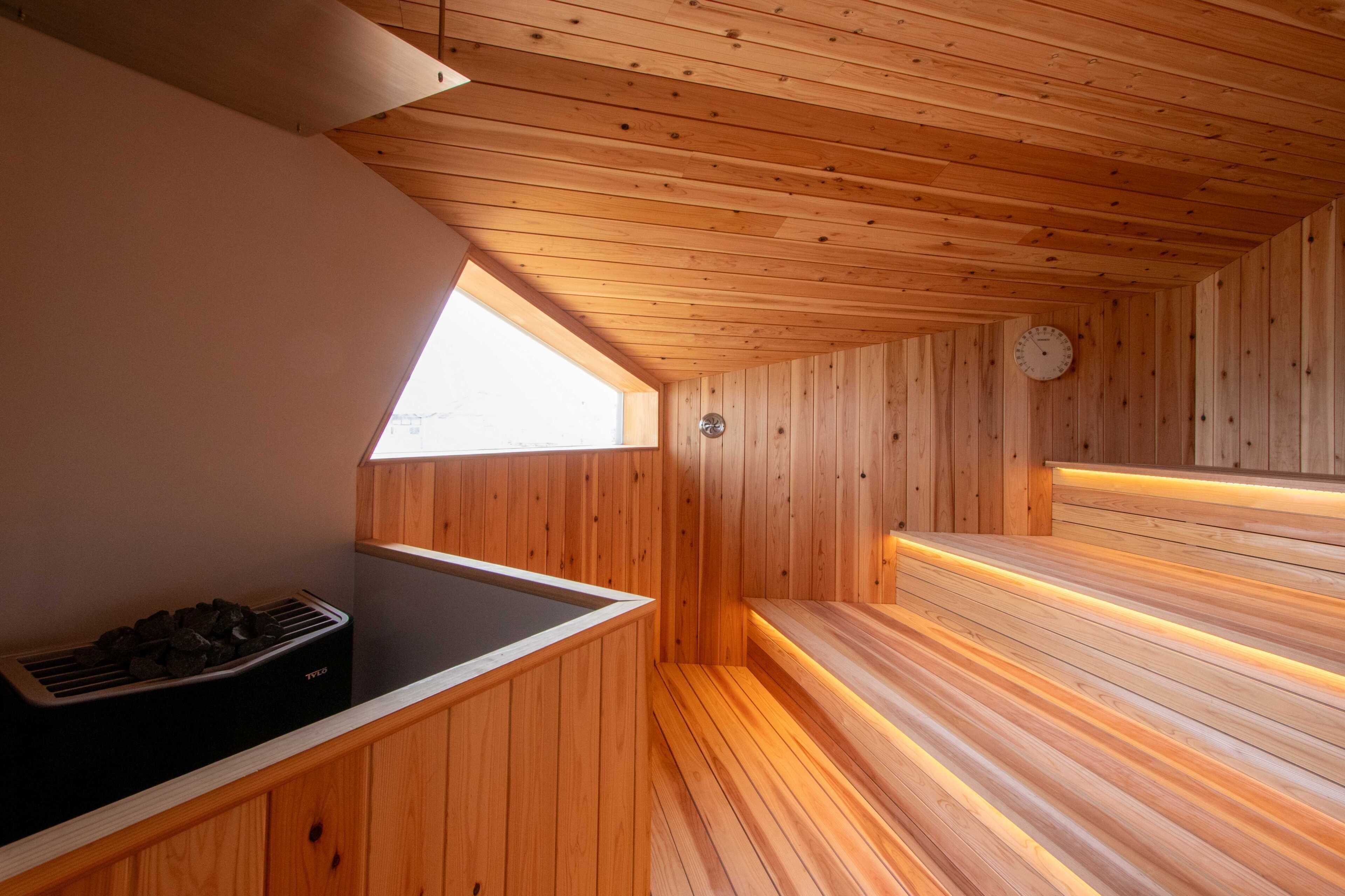 A sauna room with wooden walls and benches, a window, and a wall-mounted clock.