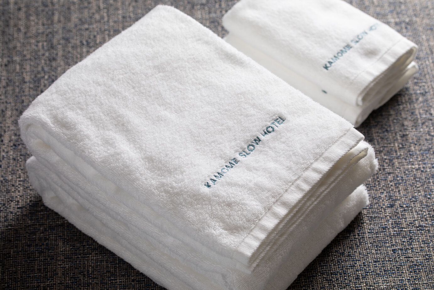 De belles serviettes blanches, soigneusement pliées, ornées d’un texte brodé sur un tissu à texture particulière.