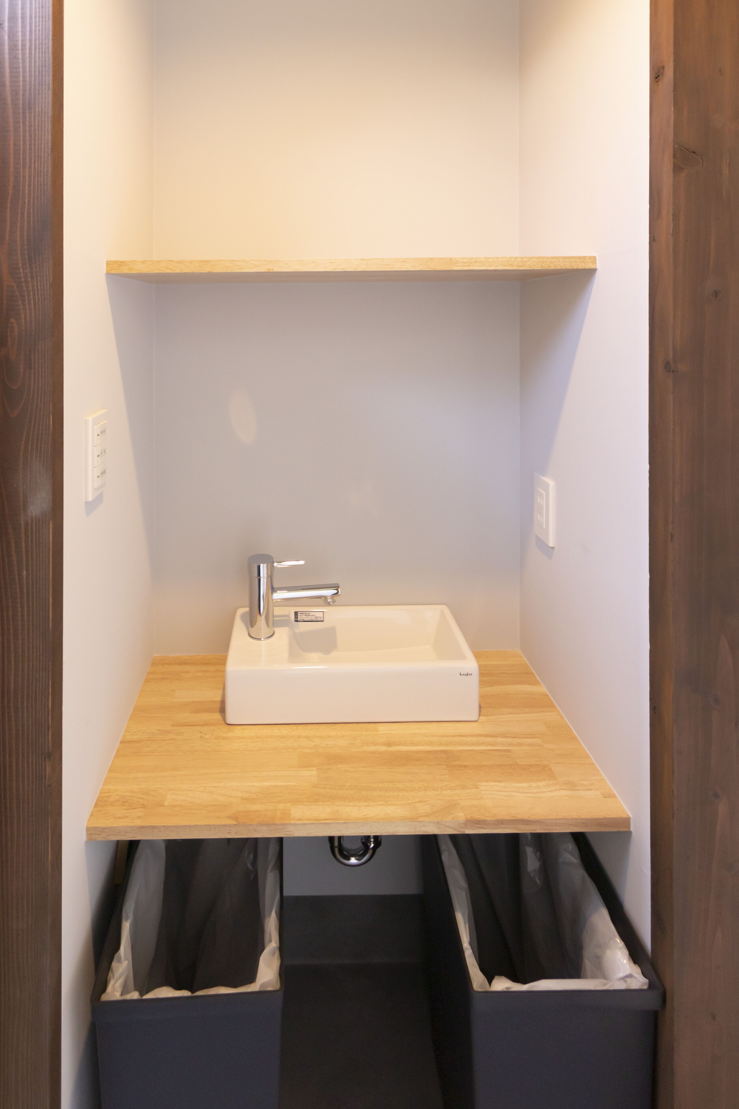 Un baño con tocador de madera, un lavamanos blanco y dos cestos de basura negros.