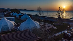 Un hotel costero con varias tiendas de campaña blancas, un comedor y vistas a la puesta de sol sobre el agua.