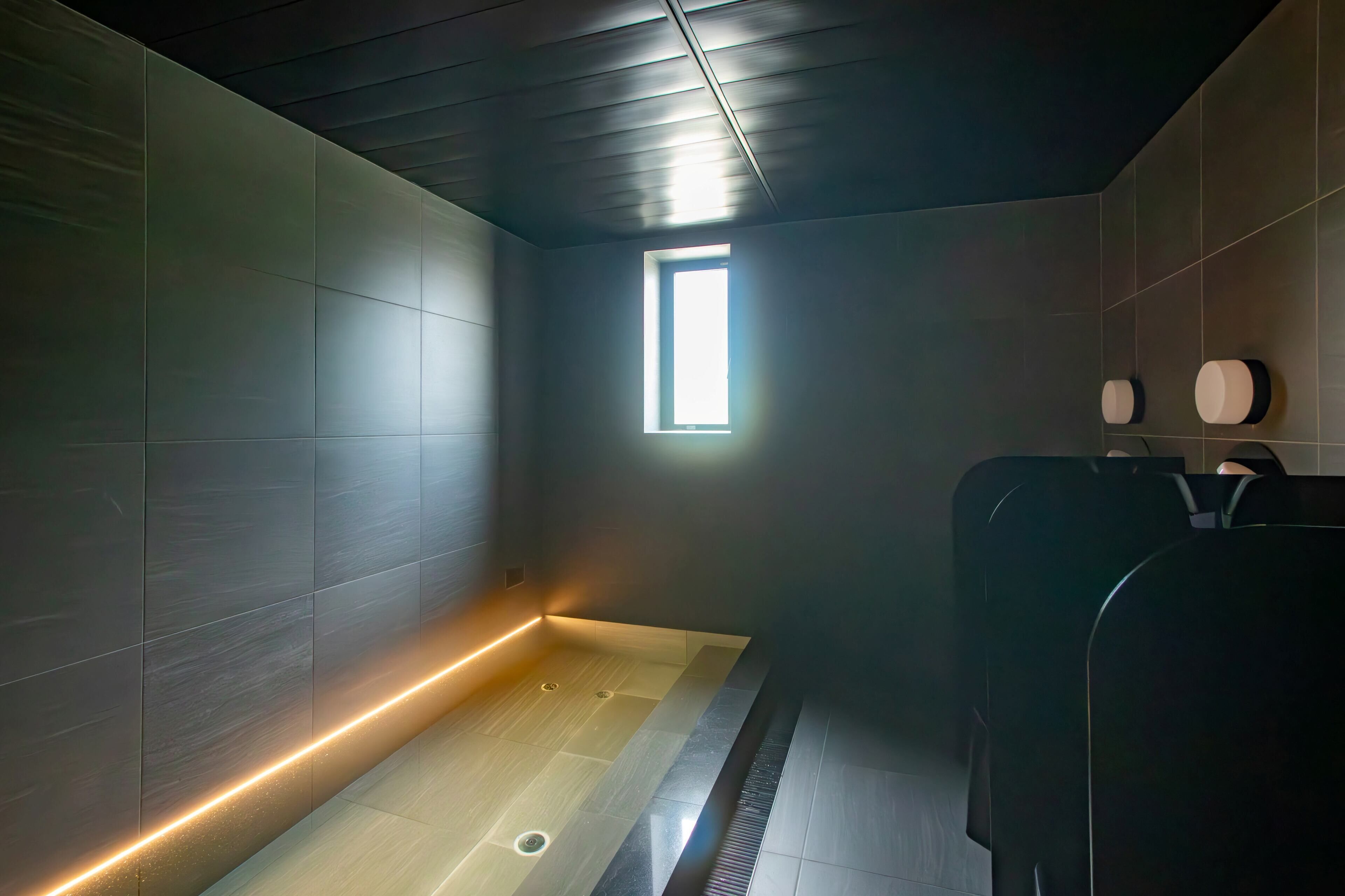 A modern bathroom with a wooden ceiling, a small window, and a heated floor.