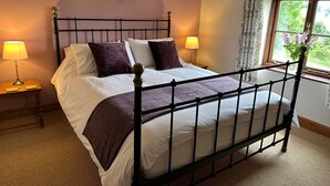 A bed with a headboard, two bedside tables, a window with curtains, and a wall-mounted heart decoration. - Old Post Office Barn (Leek)