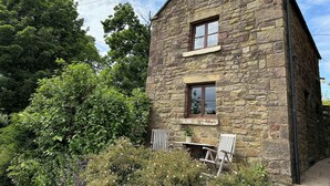 A stone building with a pitched roof, a window, and a door. - Old Post Office Barn (Leek)