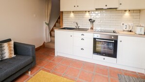 A compact kitchen with white cabinets, a built-in oven, and a sink. - Old Post Office Barn (Leek)