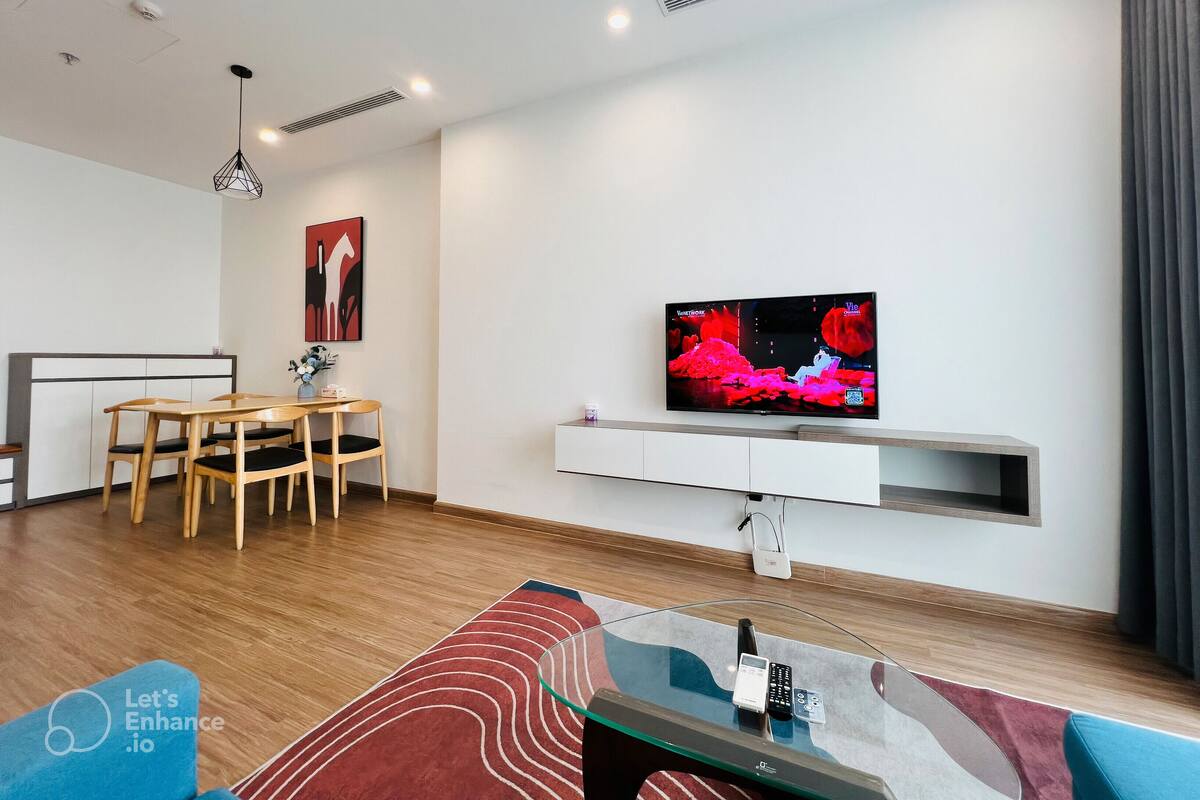 A modern living room with a flat-screen TV mounted on a white wall, wooden furniture, and a glass coffee table.