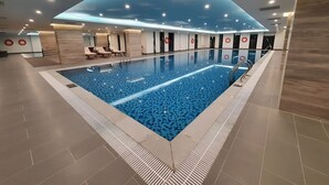 Ein großer, überdachter Pool mit blau mosaikverziertem Boden, umgeben von Liegestühlen und einer Decke im Stil eines Himmels.