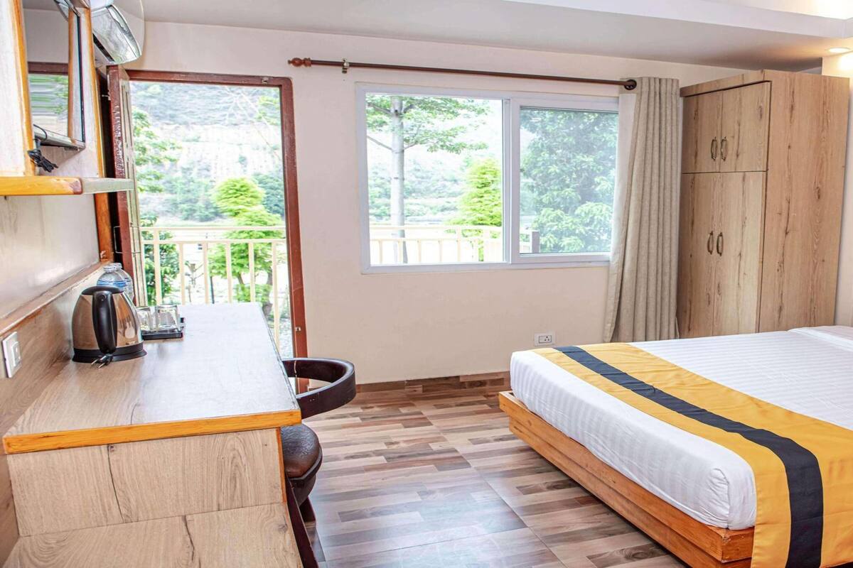 Ein Schlafzimmer mit Bett, Schreibtisch, Stuhl, Kleiderschrank und einem Fenster mit Blick auf Grünflächen.