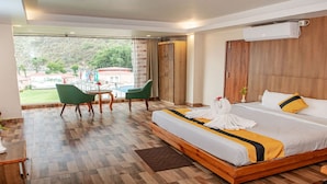 A hotel room with a large bed, a wooden headboard, a small table with chairs, and a view of the outdoors. - MeroStay 259 KB Resort (Purano Jhangajholi)