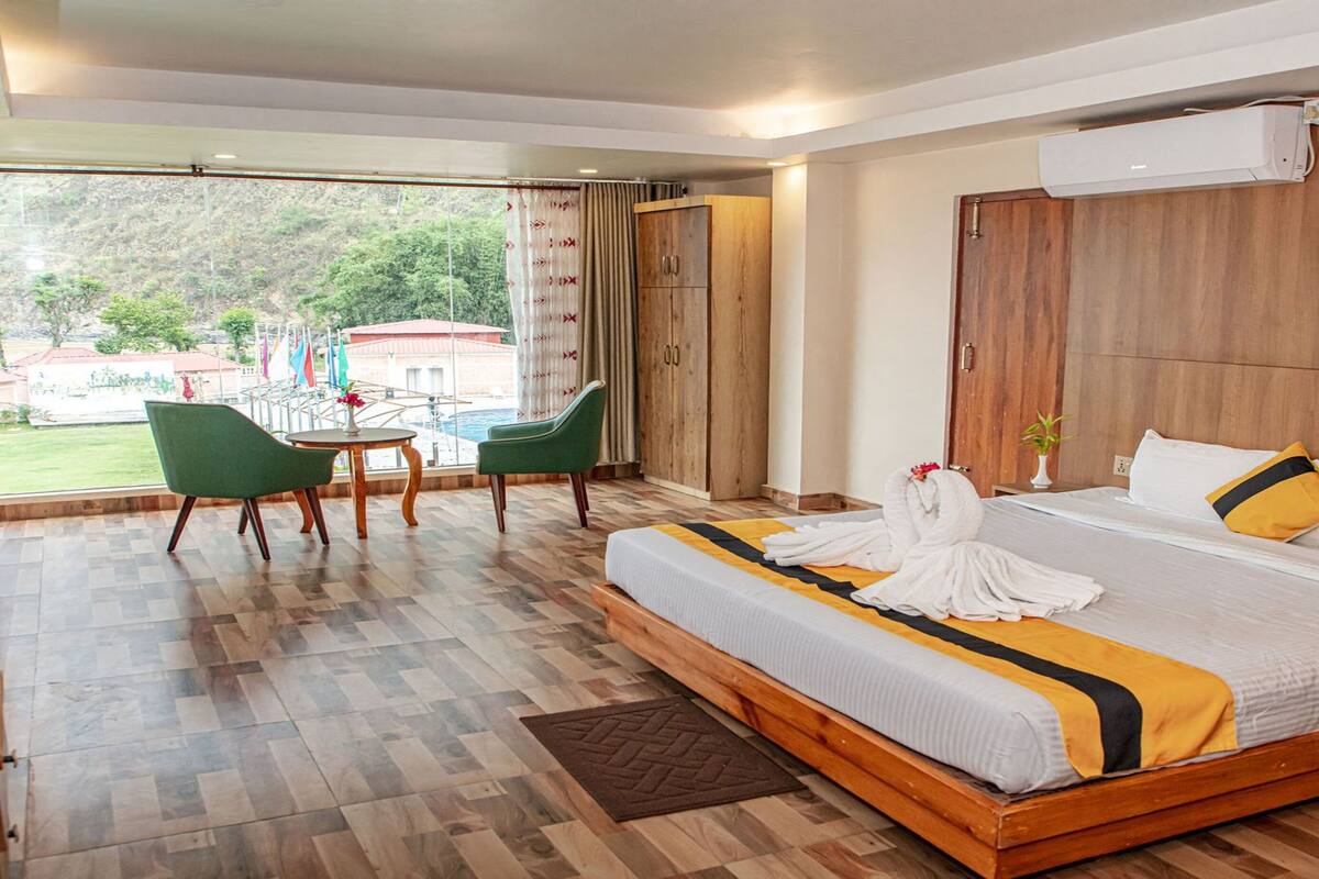 Ein Hotelzimmer mit einem großen Bett, einem Holzkopfstück, einem kleinen Tisch mit Stühlen und Blick ins Freie.