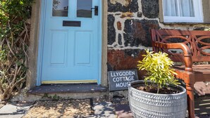 L’entrée d’un chalet avec une porte bleue, un mur de pierres, un banc et une pancarte indiquant : « Llygoden Cottage Mouse ».