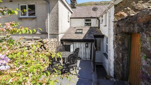 Une ruelle étroite avec un petit patio comprenant une table et des chaises, un mur de pierre et un bâtiment doté d’une cheminée.