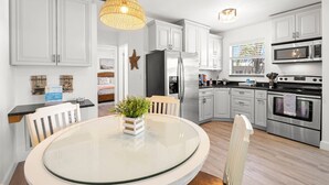 Una cocina moderna con armarios blancos, electrodomésticos de acero inoxidable y una mesa redonda de vidrio con sillas.