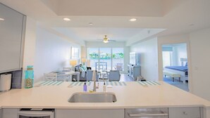 A modern kitchen with a central island, a dining area with a table and chairs, and a view of the cityscape through large windows. - Clearwater Beach Waterfront Condo w/ Boat Slip (Clearwater)