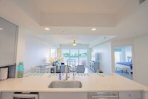 A modern kitchen with a central island, a dining area with a table and chairs, and a view of the cityscape through large windows.