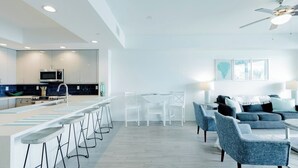 A modern kitchen with a central island, white dining area, and seating with a ceiling fan. - Clearwater Beach Waterfront Condo w/ Boat Slip (Clearwater)