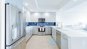 A modern kitchen with stainless steel appliances, white cabinetry, and a blue backsplash. - Clearwater Beach Waterfront Condo w/ Boat Slip (Clearwater)