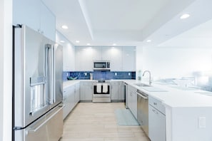 A modern kitchen with stainless steel appliances, white cabinetry, and a blue backsplash.