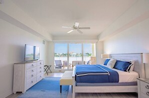 A hotel room with a bed, a TV, a ceiling fan, a balcony with chairs, and a view of the city. - Clearwater Beach Waterfront Condo w/ Boat Slip (Clearwater)