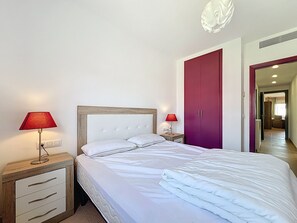 A hotel room with a bed, two bedside lamps, a wardrobe, and a hallway leading to another room.