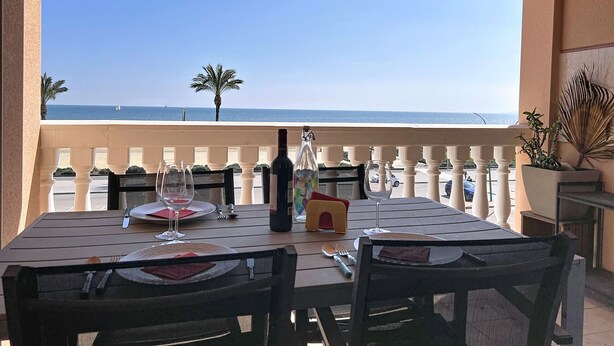 A table set for two with a view of the sea, a palm tree, and a potted plant.