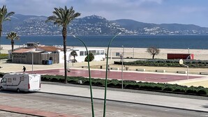 A coastal view with a beach bar, a parking lot, and a mountain in the background.