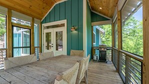 Um deck de madeira com mesa e cadeiras, churrasqueira e vista para o exterior.