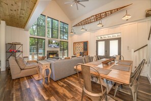 A spacious living area with a large wooden dining table, a gray sofa, and a fireplace.