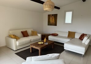 Uma sala de estar moderna com dois sofás brancos, uma mesa de centro de madeira e um quadro grande na parede.