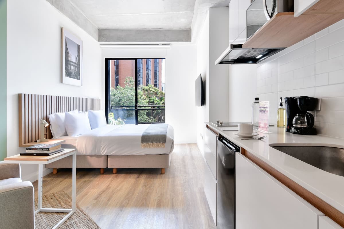 Ein modernes Hotelzimmer mit Bett, Nachttisch und Blick auf die Stadt durch große Fenster.