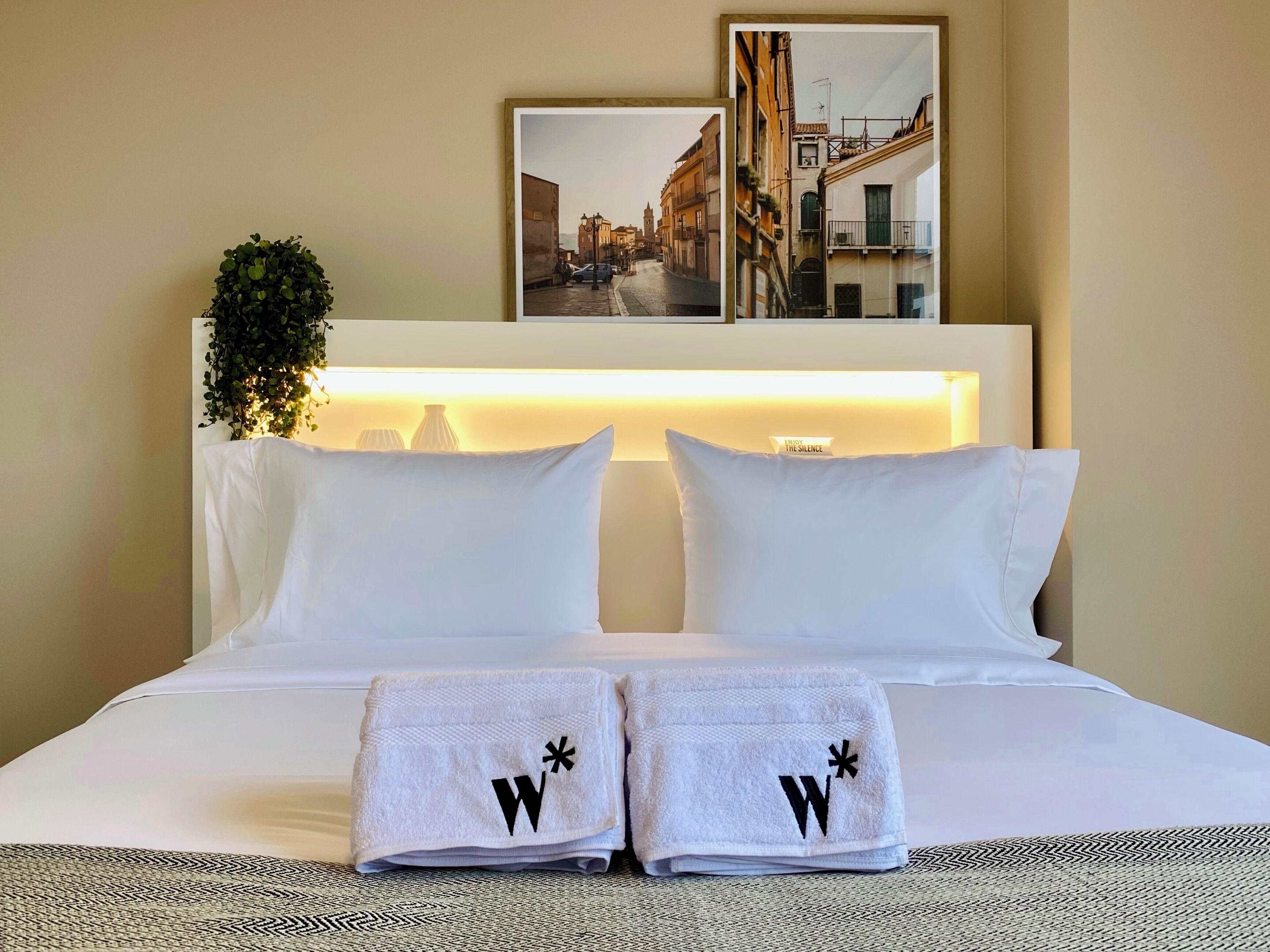 A neatly made bed with white linens, two pillows, and two folded towels with a logo.