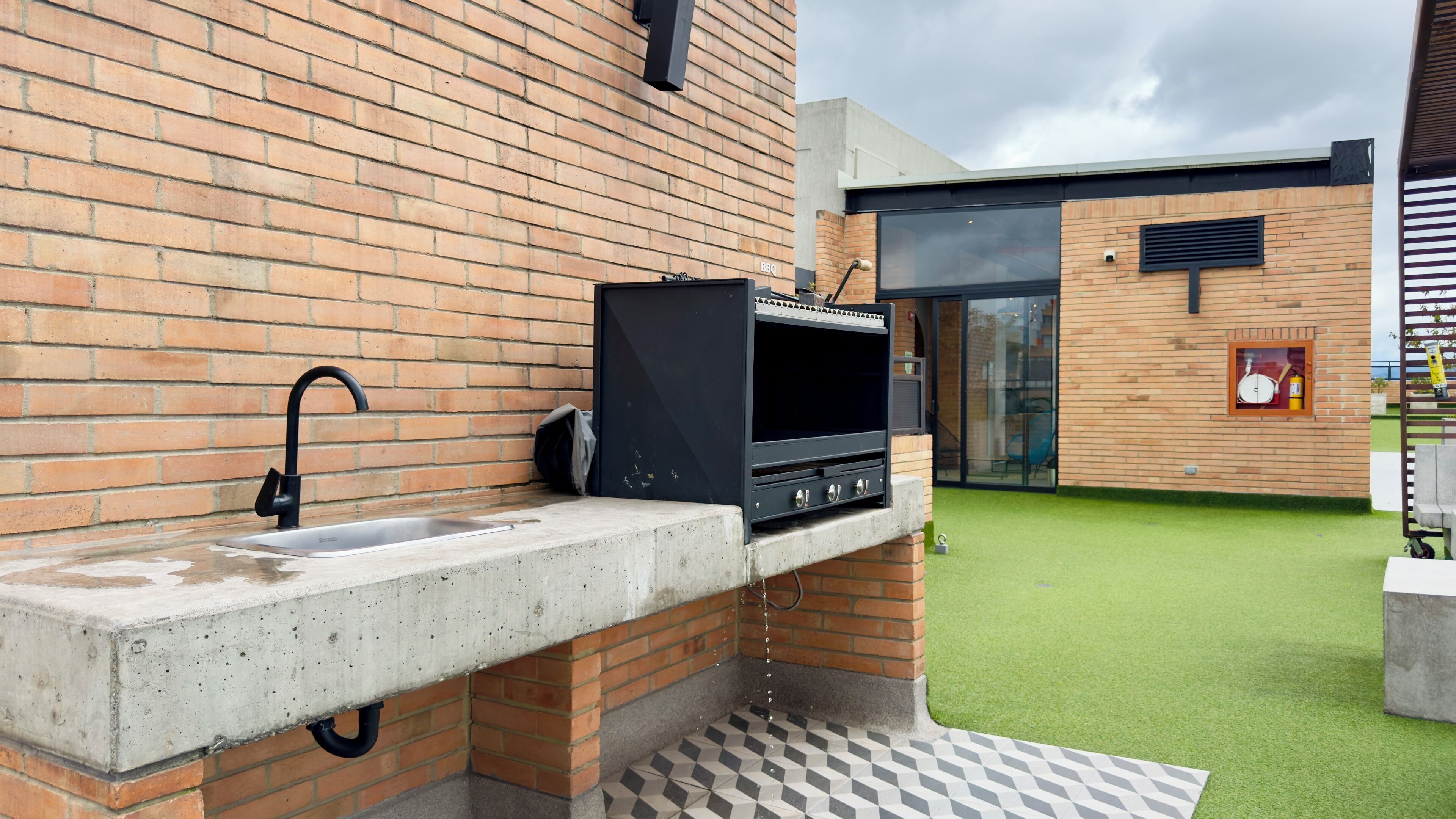 An outdoor kitchen with a grill, sink, and a patio area with artificial grass.