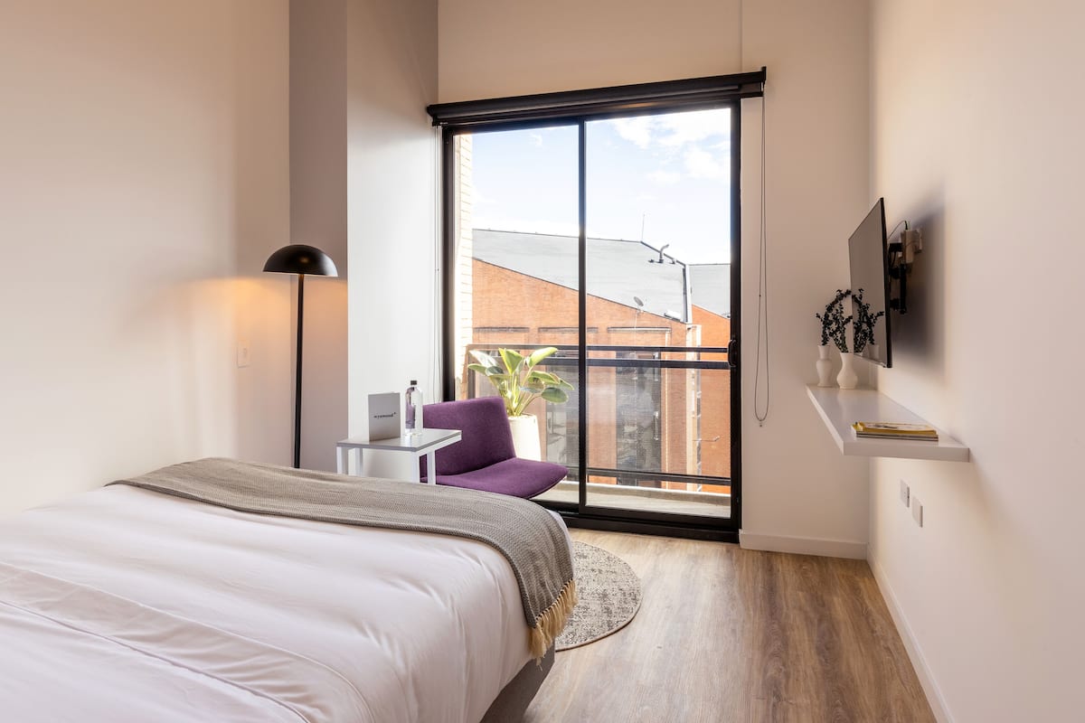 Ein modernes Schlafzimmer mit großem Fenster, einem Bett, einem kleinen Tisch und einem Stuhl.