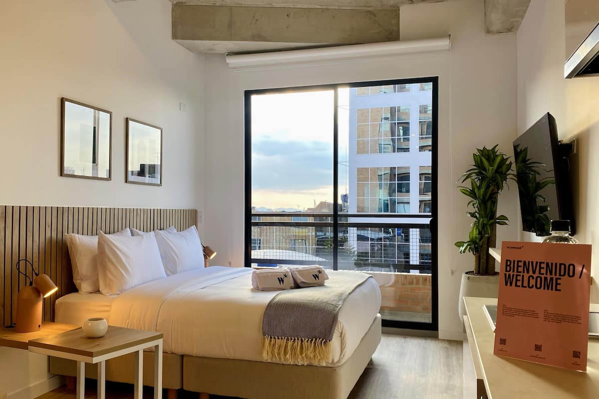 Ein modernes Hotelzimmer mit einem großen Bett, einem Schreibtisch, einem kleinen Tisch, einem Fernseher und einem Balkon mit Blick auf die Stadt.