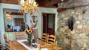 A wooden dining table with six chairs, a chandelier, and a stone wall with a fishing net.