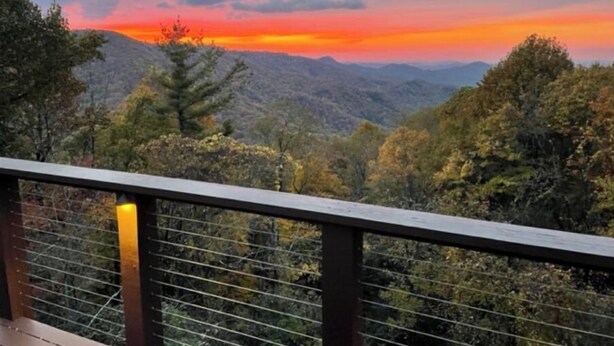 A scenic view from a wooden deck overlooking a mountainous landscape with a sunset.