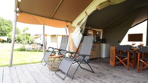 Un espace extérieur abrité par une tente, doté d’une terrasse en bois, d’une table avec des chaises et d’un panier en osier.