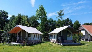 Deux petites cabanes mobiles, dotées d’auvents, sont installées sur un terrain herbeux, avec des arbres en arrière-plan.