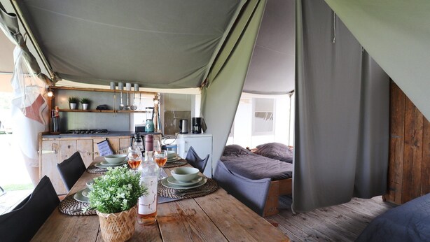 Un hébergement confortable en forme de tente, comprenant une table à manger en bois pour deux personnes, un coin cuisine et un espace de couchage agréable.