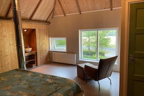 Un dormitorio con cama, ventana, una silla y un armario de madera.