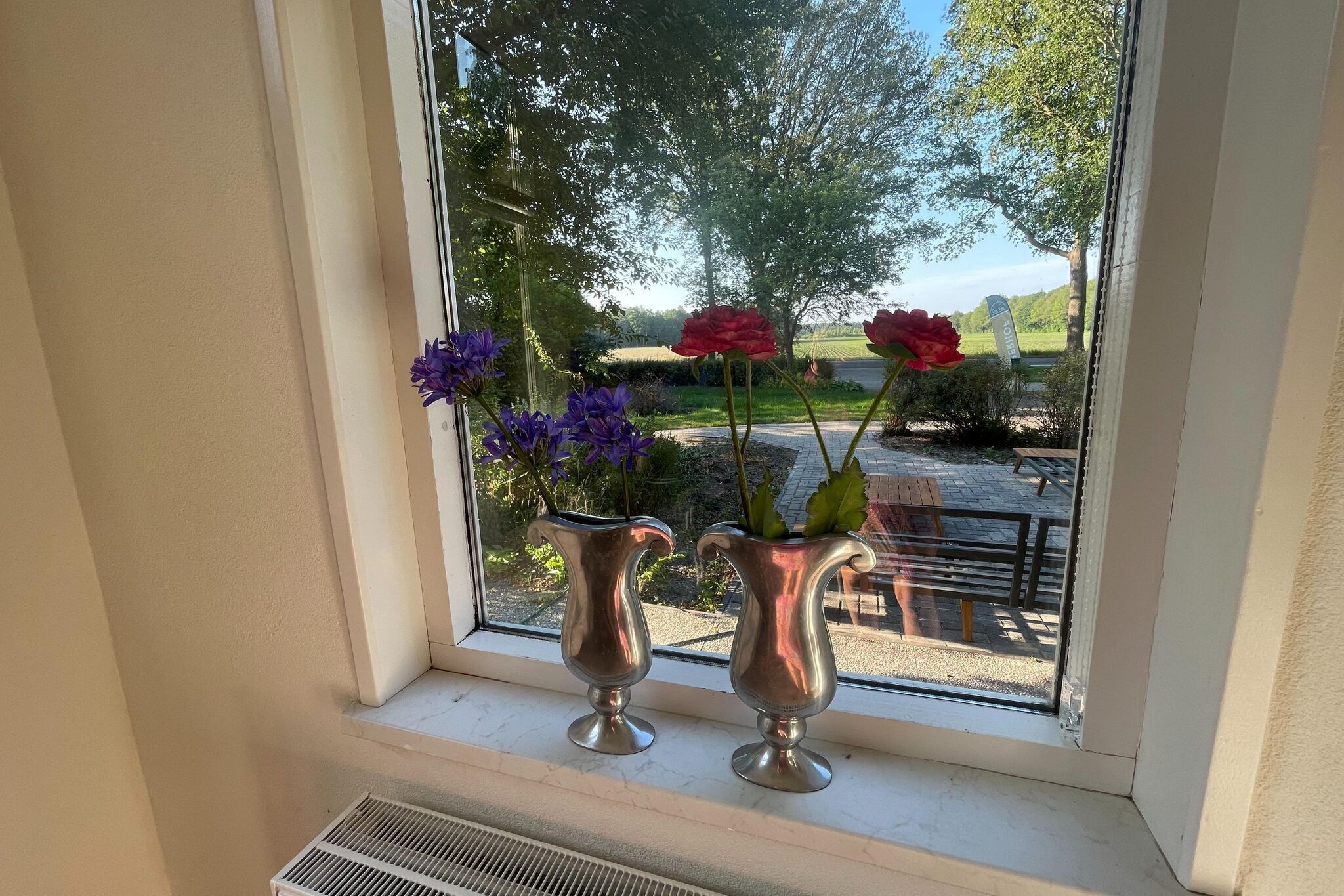 Två silvervaser med blommor står på en fönsterbräda.
