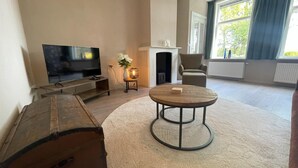A living room with a television, a fireplace, a round table, and a large wooden chest. - Vacation home in Schoonloo with terrace (Schoonloo)