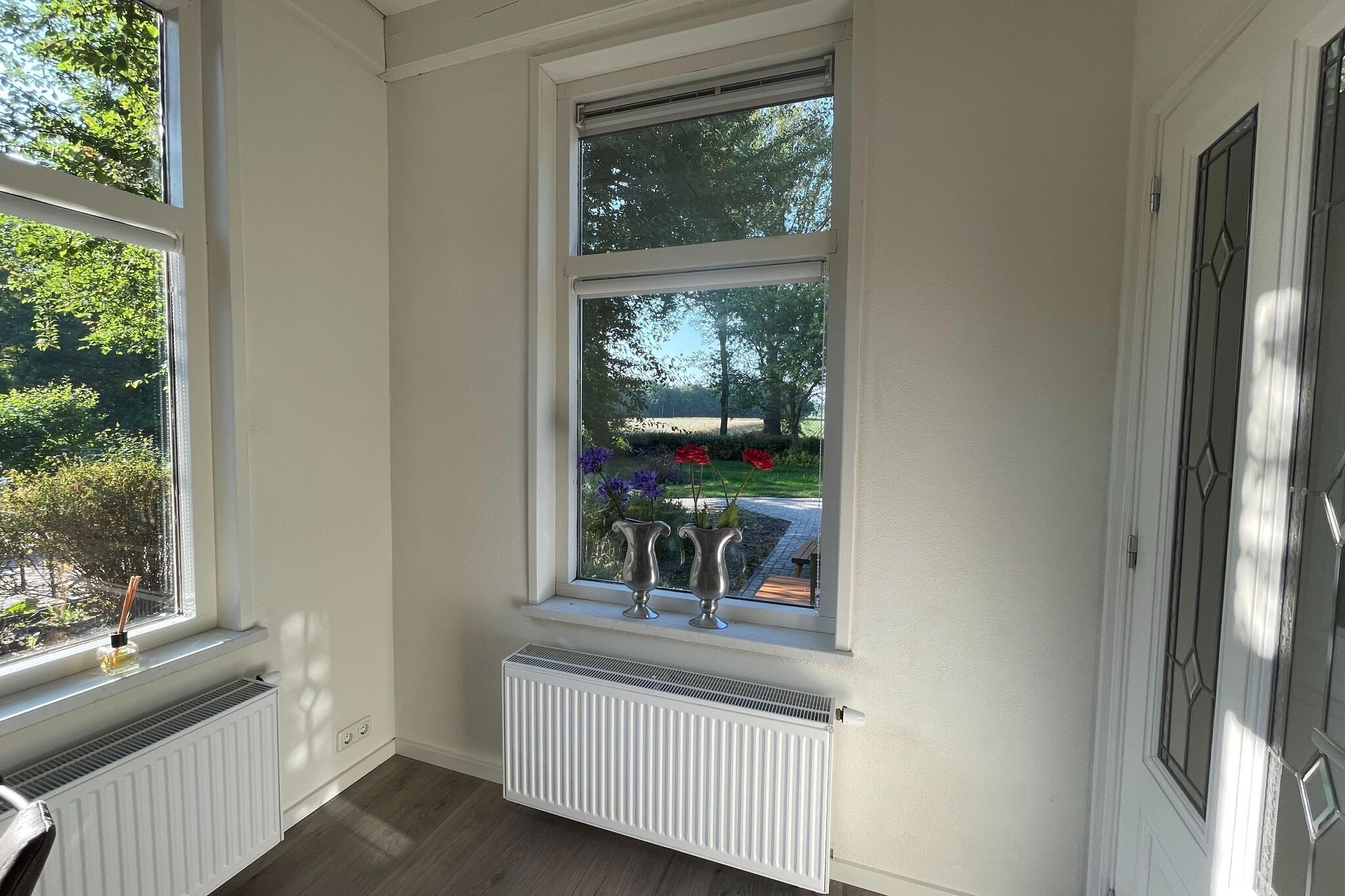 Une pièce dotée d’une grande fenêtre, d’un radiateur et d’une porte ornée d’un panneau de verre décoratif.