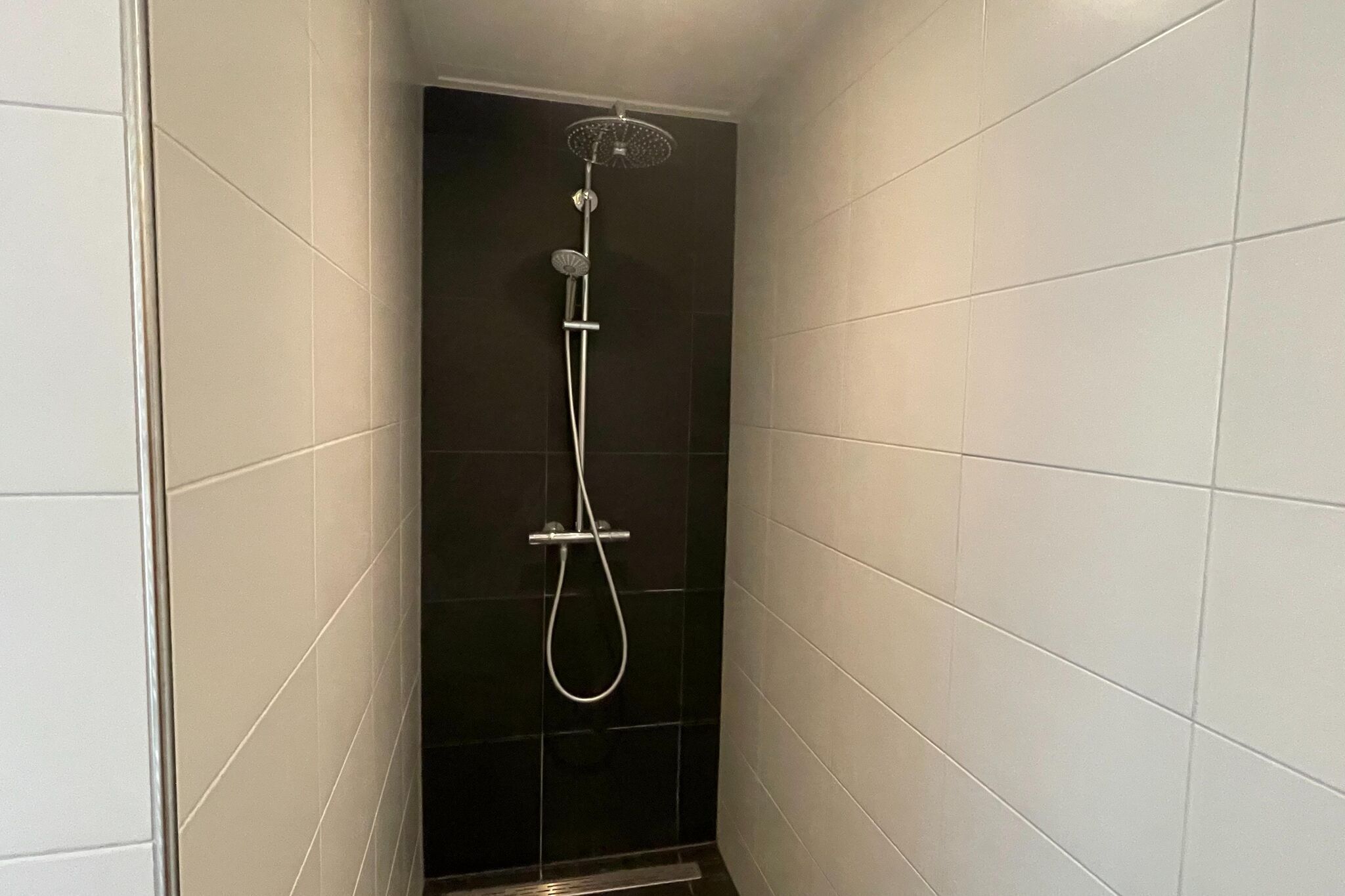 A shower with a handheld showerhead and a wall-mounted rain showerhead in a tiled bathroom.