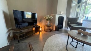 A living room with a flat-screen TV, a fireplace, a round coffee table with pumpkins, and a white vase with flowers. - Vacation home in Schoonloo with terrace (Schoonloo)