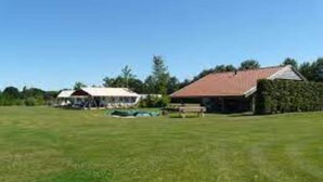 A grassy field with two buildings, one with a red roof and another with a white roof, surrounded by trees.