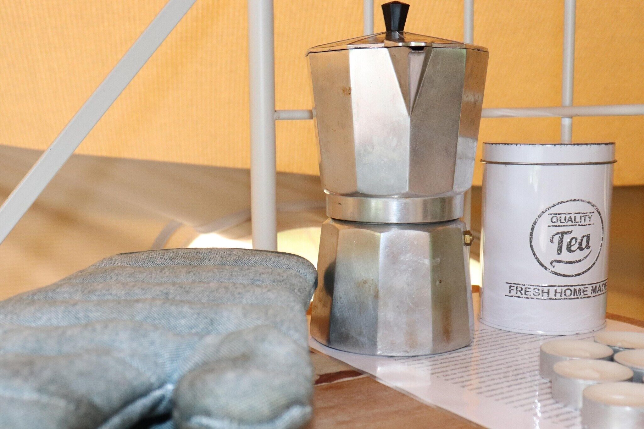 A coffee maker, a canister labeled "Quality Tea," and a cloth napkin on a table.
